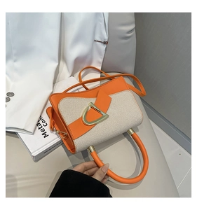 Detail of orange and beige handbag featuring a stylish gold D-ring buckle and crossbody strap