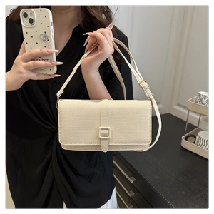 Detail showing the fine textured cream fabric and square buckle on the crossbody bag