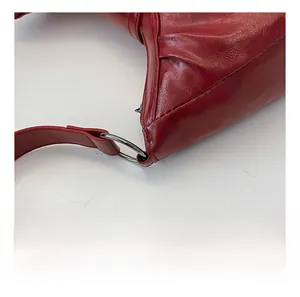 Close-up of silver metal ring and stitch detail on a glossy red leather shoulder bag