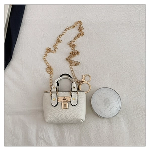 Nahaufnahme eines weißen Mini-Taschenanhängers mit Goldkette und passender Puderdose