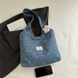 Close-up of blue denim tote bag featuring white bow heart prints and a plush cat charm