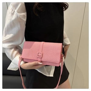 Model wearing a pink textured crossbody bag with a square buckle and adjustable strap