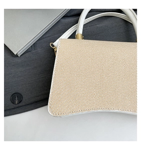 Detail of khaki woven crossbody bag with white leather trim and gold hardware accents