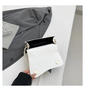 Detailed top view of white crossbody bag with asymmetric flap and dual gold magnetic buckles