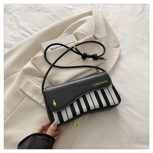 Detail of piano key crossbody bag with I LIKE MUSIC text on a beige blazer