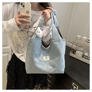 Detail of light blue embroidered tote bag with bow patterns and plush charm accessory