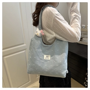 Close-up of light blue canvas tote bag with white bow pattern and plush kitten charm