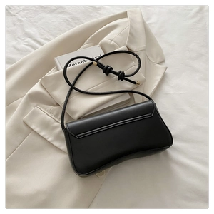 Detail of black leather handbag featuring gold hardware accents on a beige blazer