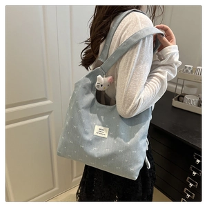 Detail of light blue canvas tote with bow print and cute plush charm on shoulder