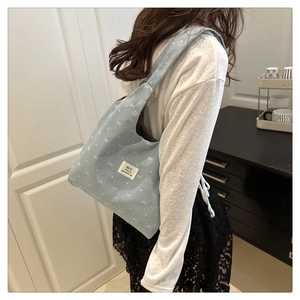 Detail shot of a light blue canvas shoulder bag with white bow embroidery and logo tag