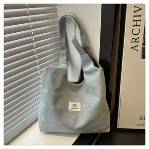Detail showing light blue denim tote bag texture with white bow patterns and woven label