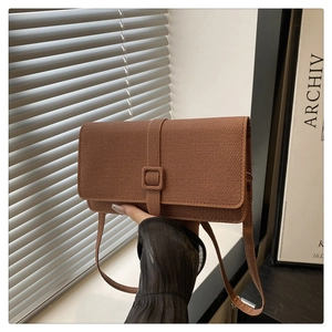 Detail of a brown woven texture rectangular flap crossbody bag held by hand