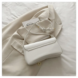 Flat lay of a white minimalist shoulder bag with knot strap on a beige suit background