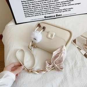 Cream shoulder bag with silk scarf strap and plush charm on white aesthetic background
