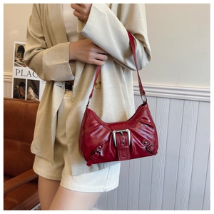 Detail of red vintage underarm bag with silver buckles worn over a beige suit