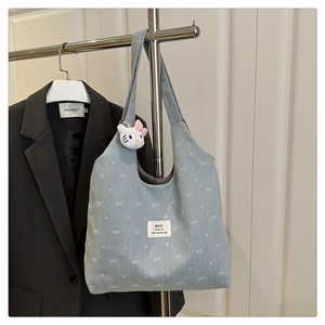 Detail of light blue denim tote with white bow pattern and cute kitty plush charm