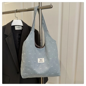 Close-up of soft denim tote bag with white bow print and woven label on a metal hanger