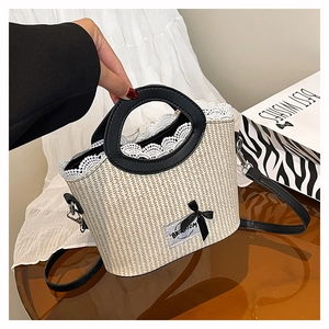 Detail van de stro emmer tas met witte kant afwerking en zwarte strik decoratie