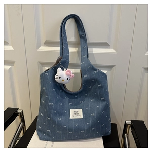 Detail of blue denim tote bag with white bow patterns and Hello Kitty plush charm