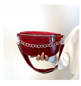 Detail of red patent leather waist bag with chunky silver chain and wide textile strap