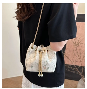 Close-up of cream woven bucket bag with floral embroidery and pearl drawstring details