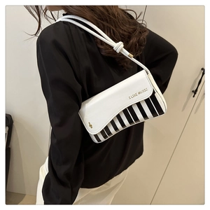 Detail of piano key handbag featuring golden music print and stylish knot leather strap