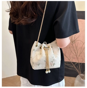 Detail of woven bucket bag with floral embroidery, gold chain, and pearl drawstring