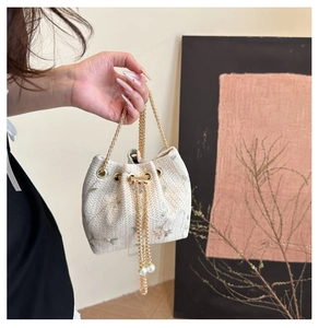 Detail of floral embroidery and pearl drawstring on beige straw bucket bag