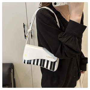 Detail of piano key pattern and golden I LIKE MUSIC slogan on white shoulder bag