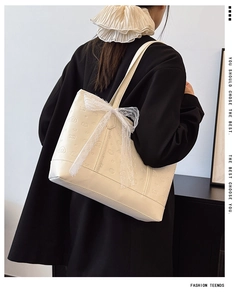 Close-up of cream leather tote bag with logo embossing and white lace bow detail