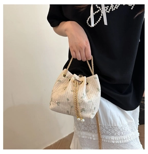 Detail view of woven straw bucket bag with floral embroidery and gold chain handle