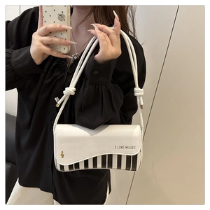Detail showing music-themed piano key pattern and gold treble clef on white shoulder bag