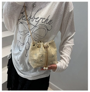 Detail of straw bucket bag with floral embroidery and pearl drawstring on model