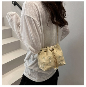 Detail of woven straw bucket bag with floral embroidery and elegant pearl drawstring