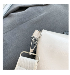 Nahaufnahme der cremeweißen Leder-Brusttasche mit silbernem Drehverschluss und breitem Gurt