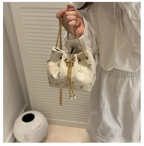 Detail of woven bucket bag featuring green floral embroidery and pearl chain drawstring