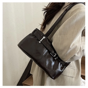 Detail of dark oil wax leather baguette bag with silver buckle on beige blazer