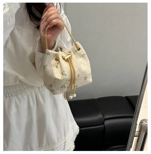 Detail of straw bucket bag with floral embroidery, gold chain, and pearl drawstring strap