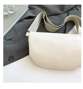 Close-up of cream crescent crossbody bag with wide canvas strap and silver metal buckle