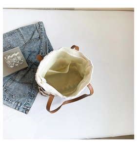 Detail view of woven tote bag showing beige texture, spacious interior, and brown leather handles