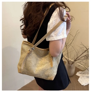 Close-up of woven straw tote bag with brown leather handles worn by a model indoors