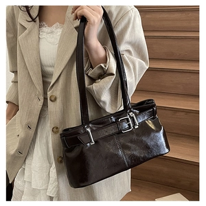 Detail of glossy dark brown baguette shoulder bag with buckle strap on a model