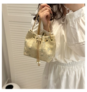 Detail shot of straw bucket bag featuring floral embroidery and pearl drawstring closure