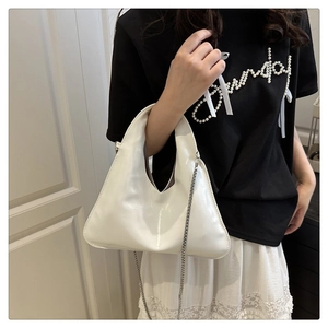 Close-up of white glossy hobo bag with silver chain strap worn by a model