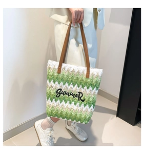 Detail of woven tote bag featuring green wave patterns and leather shoulder handles