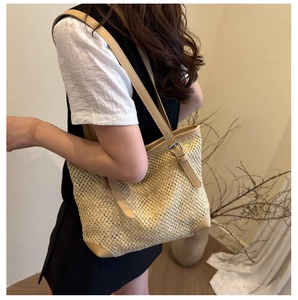 Detail of woven straw tote bag with brown adjustable leather strap and silver buckle