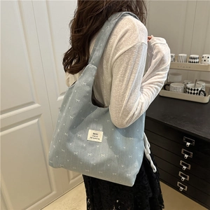 Light blue canvas tote bag with bow patterns and shoulder strap shown on a model