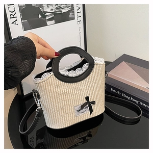 Détail d'un sac seau en paille avec dentelle, nœud noir et broderie de marque