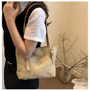 Detail of woven straw tote bag with faux leather straps and metal buckle accents