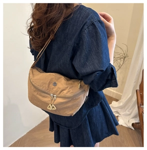 Detailed view of a tan washed fabric crossbody bag with metallic zippers and branding